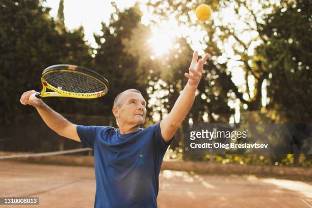 serious and concentrated on game tennis player with racquet before pitch. active senior man - tennis stock-fotos und bilder