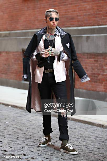 Chris Lavish wears Fendi sunglasses, a black Ears of Buddha Sustainably Stylish Upcycled Duster trench coat, a pink satin Ears of Buddha shirt, a...