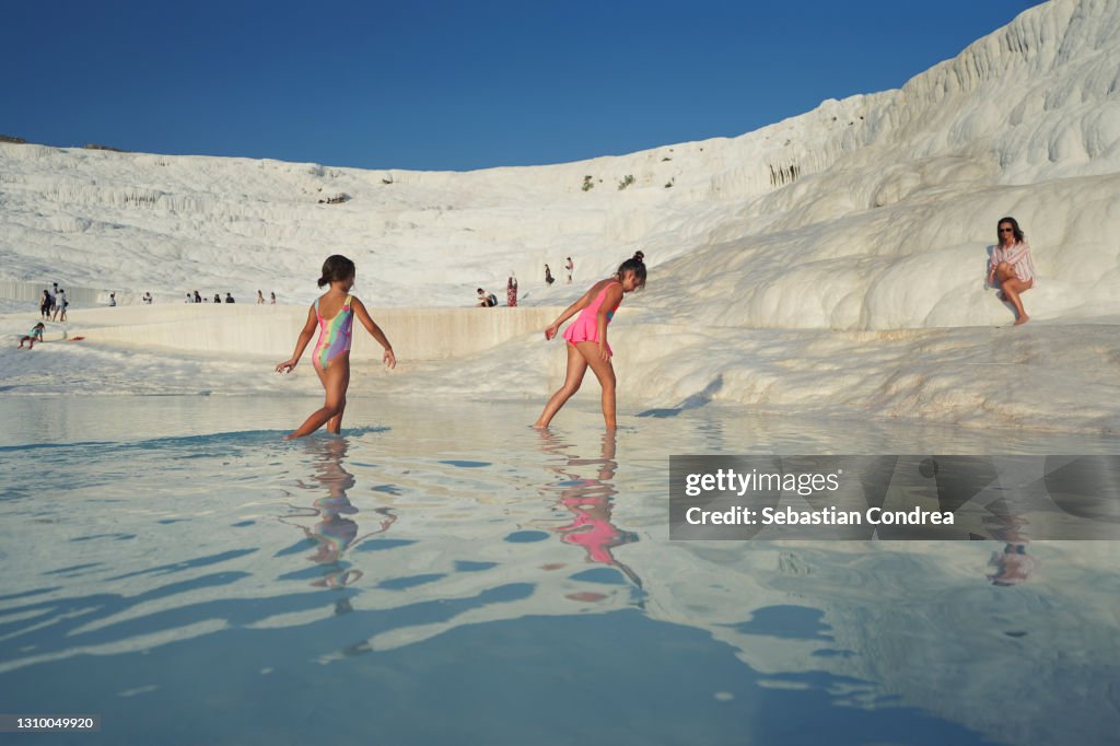 Tourist girls are walking and playing on travertines of Pamukkale. Pamukkale's terraces are made of travertine.