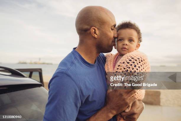 father kissing baby girl wrapped in blanket on beach - babyhood - fotografias e filmes do acervo