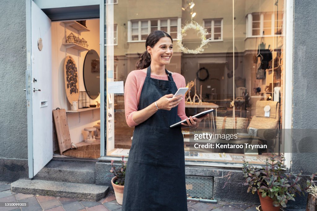 Smiling female entrepreneur with smart phone and digital tablet outside store