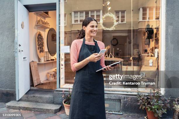 smiling female entrepreneur with smart phone and digital tablet outside store - owner bildbanksfoton och bilder