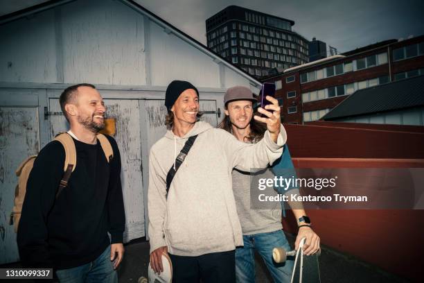 smiling male friends taking selfie on smart phone against shed on street - 30 39 years stock pictures, royalty-free photos & images