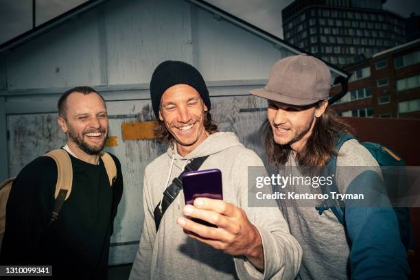 happy male friends taking selfie on smart phone against shed on street - nur erwachsene stock-fotos und bilder