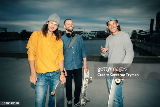 portrait of smiling male friends with skateboards against canal at dusk - kommunikationskanäle stock-fotos und bilder