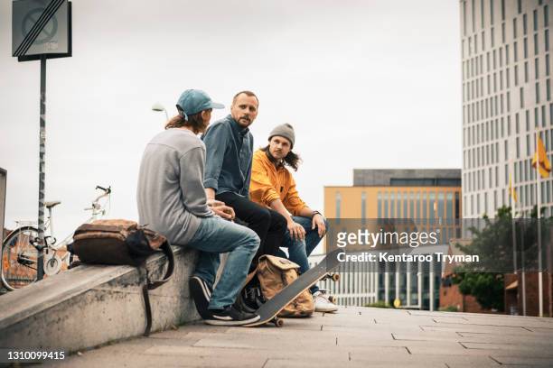 male friends talking with each other while sitting on retaining wall - nur erwachsene stock-fotos und bilder