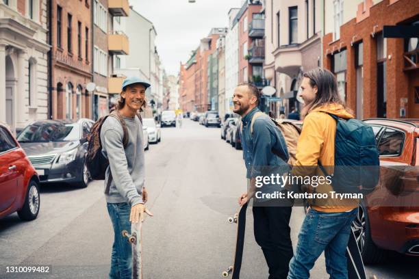 happy friends talking while standing with skateboards on street in city - nur erwachsene stock-fotos und bilder