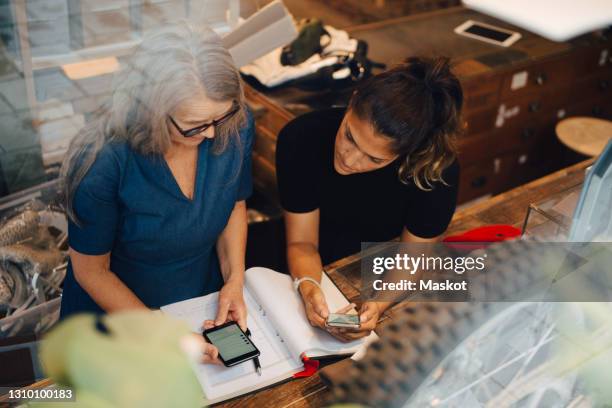 high angle view of female colleagues discussing over smart phone in retail store - future retail stock pictures, royalty-free photos & images