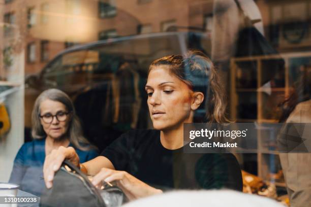female colleagues seen through glass working in clothing store - clothing store stock pictures, royalty-free photos & images