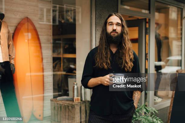 portrait of male entrepreneur with coffee cup against clothing store - langes haar stock-fotos und bilder