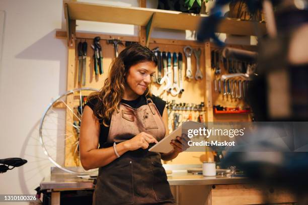 smiling female owner using digital tablet at bicycle workshop - mechanic computer stock pictures, royalty-free photos & images