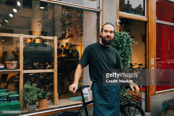 portrait of smiling male mechanic by bicycle outside retail shop - bike shop stockfoto's en -beelden