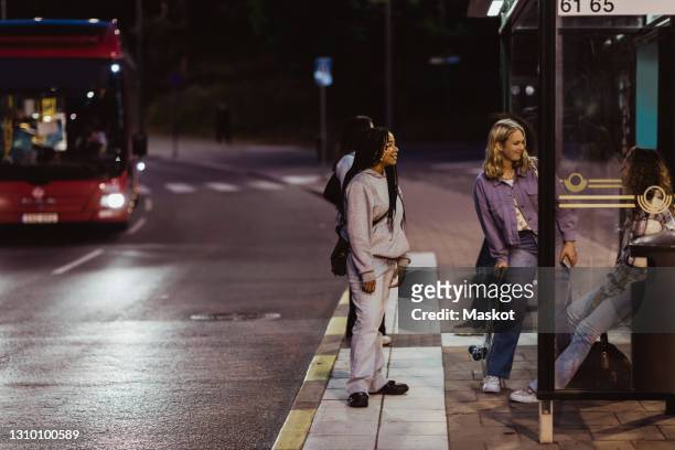 female friends sitting on bus stop at night - bus stop stock pictures, royalty-free photos & images