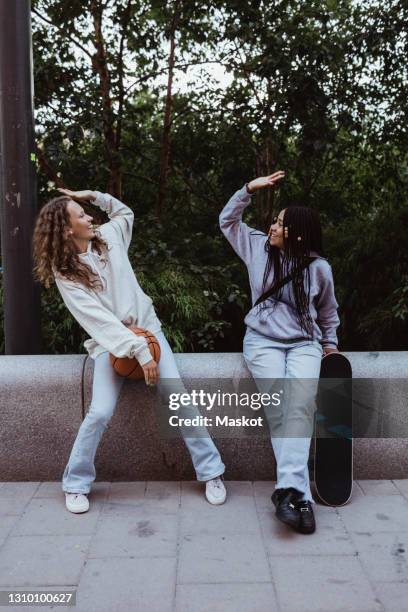 female friends doing high-five while sitting on retaining wall at footpath - girl sitting stock-fotos und bilder