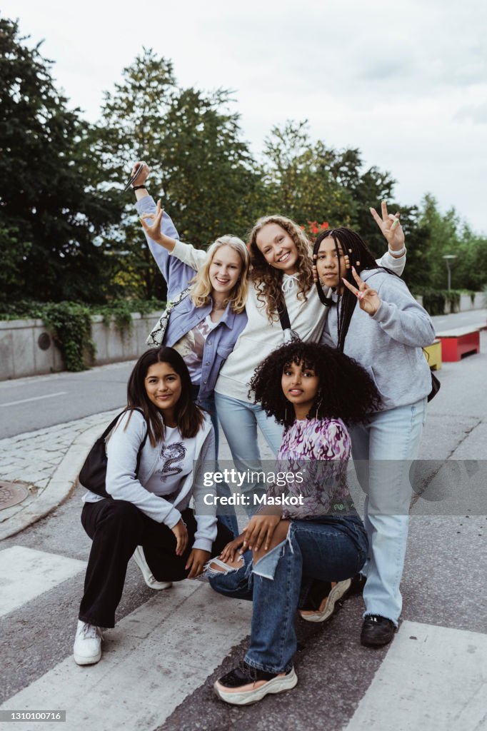 Portrait of female friends gesturing with peace sign on street