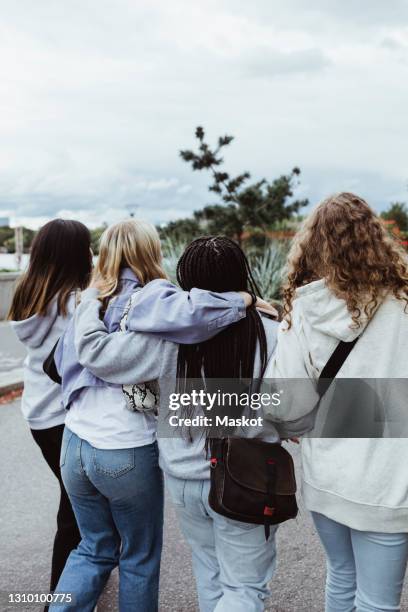 rear view of friends with arms around walking on footpath - vestito nero foto e immagini stock
