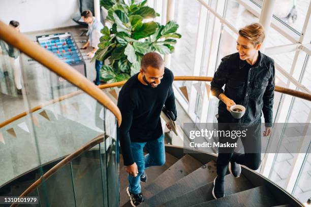 smiling male and female climbing steps in office - staircase photos et images de collection