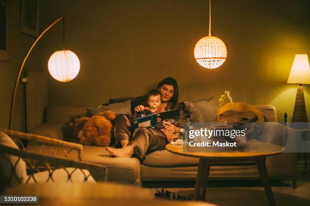 mother with baby girl reading book in living room - mum sitting down with baby stockfoto's en -beelden