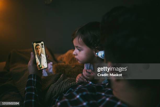 sick man consulting online through video call on smart phone with female doctor at home - screening of a24s hot summer nights red carpet stockfoto's en -beelden