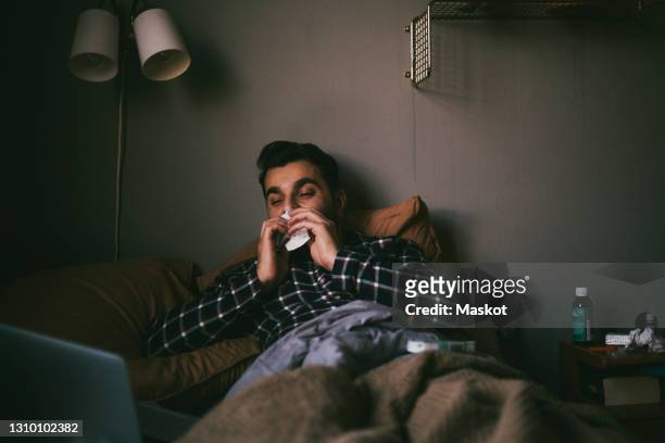 man blowing nose while having online consultation at home - man flu foto e immagini stock