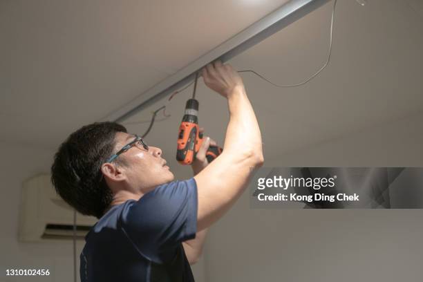 asian chinese electrician man installing electric lamp on ceiling using cordless drill. - asian ceiling stock pictures, royalty-free photos & images