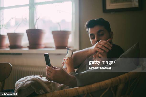 father checking temperature of son while sitting in living room at home - fieber stock-fotos und bilder