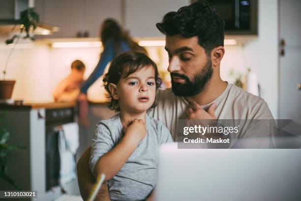 father and son taking online advice through laptop at home - stockholm syndrome stock pictures, royalty-free photos & images