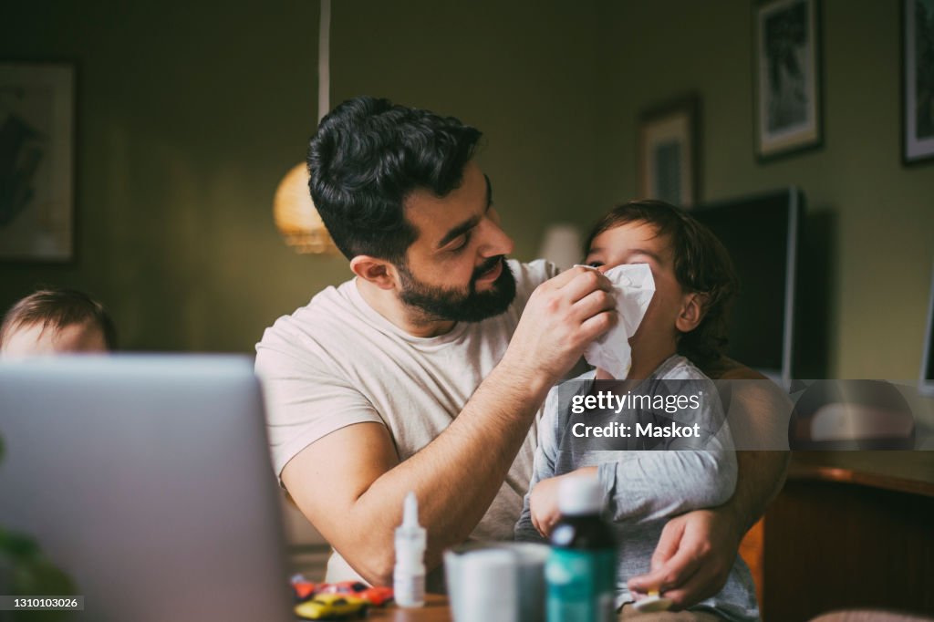 Father blowing nose of son in living room