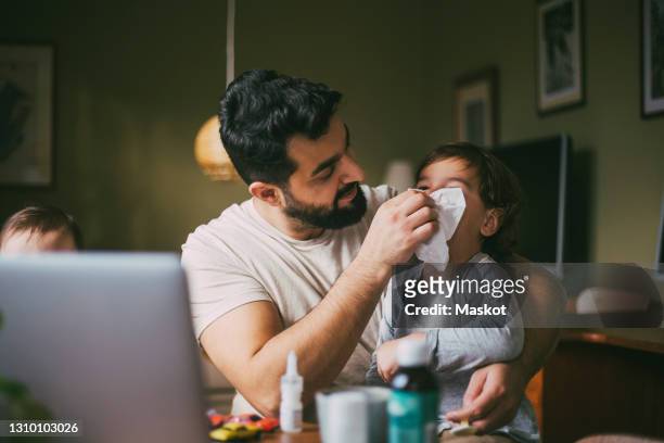 father blowing nose of son in living room - sonarse fotografías e imágenes de stock