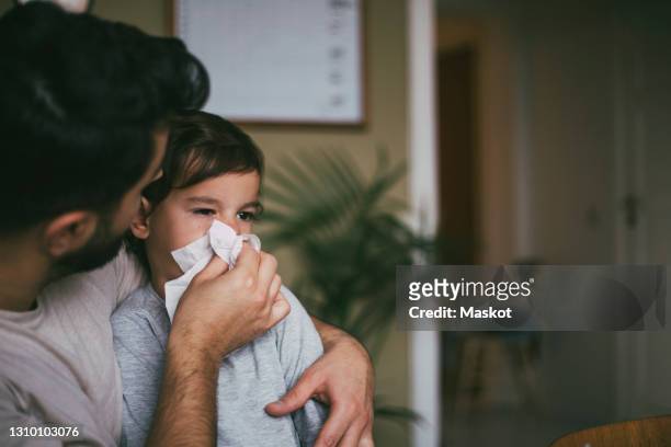 father blowing nose of sick son at home - sick kid fotografías e imágenes de stock