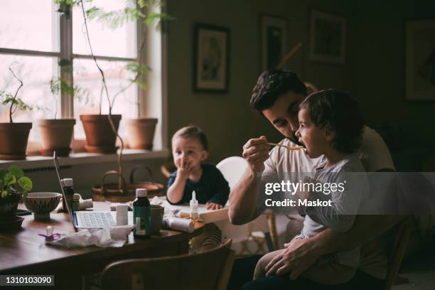 father feeding son in living room at home - baby feeding fotografías e imágenes de stock