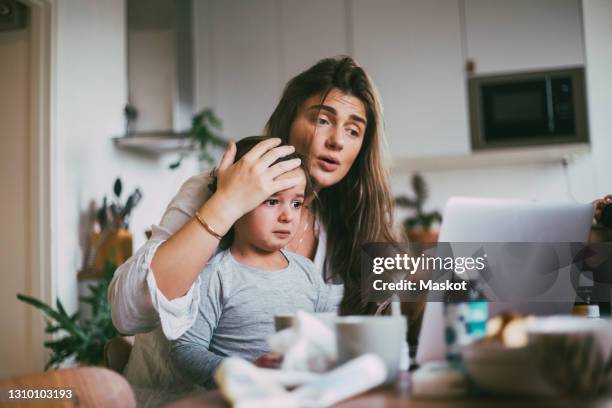 mother with sick son taking advice on video call at home - malattia foto e immagini stock