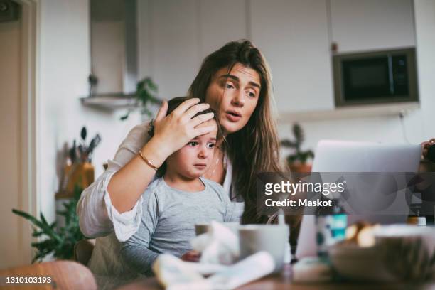 mother with sick son taking advice on video call at home - ziek stockfoto's en -beelden