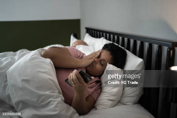 woman in bed checking smartphone - waking up in bed stock pictures, royalty-free photos & images