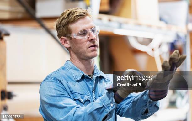 man standing in workshop putting on work gloves - work glove stock pictures, royalty-free photos & images