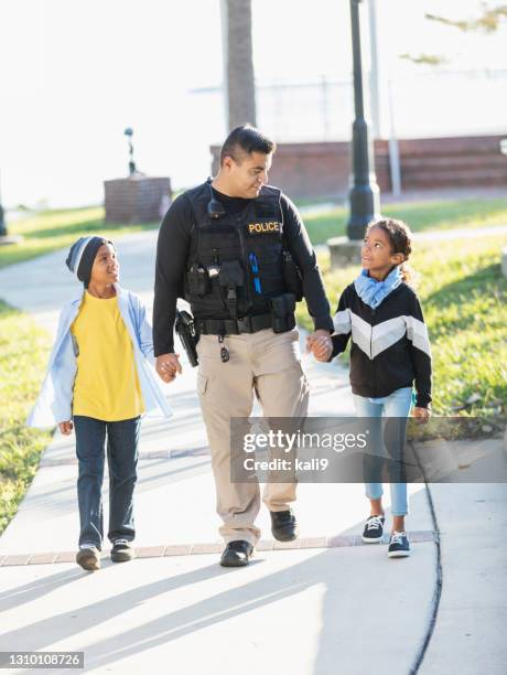 police officer in community, walking with two children - police force stock pictures, royalty-free photos & images