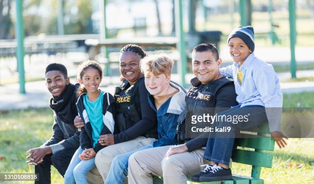 two police officers sitting with children on park bench - police stock pictures, royalty-free photos & images