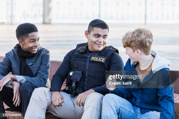 police officer in community, sitting with two youths - police officer smiling stock pictures, royalty-free photos & images