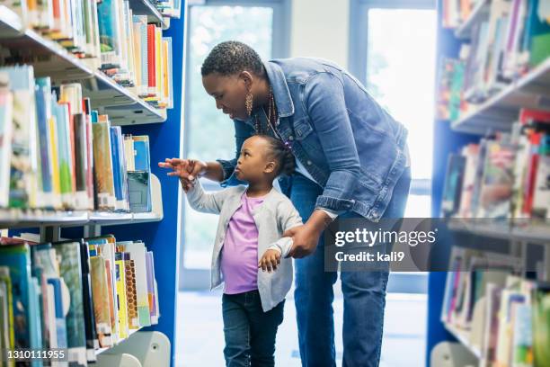 meisje met moeder die boeken op bibliotheekboekenplank bekijkt - differential focus education reach stockfoto's en -beelden