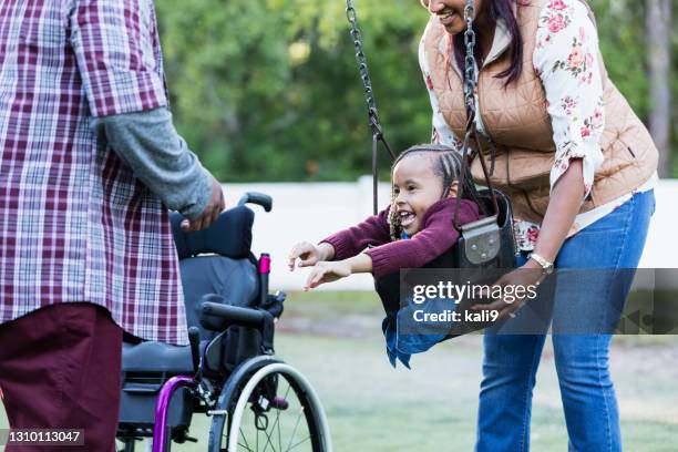 parents, daughter with disability playing in swing - playground equipment happy parent stock pictures, royalty-free photos & images