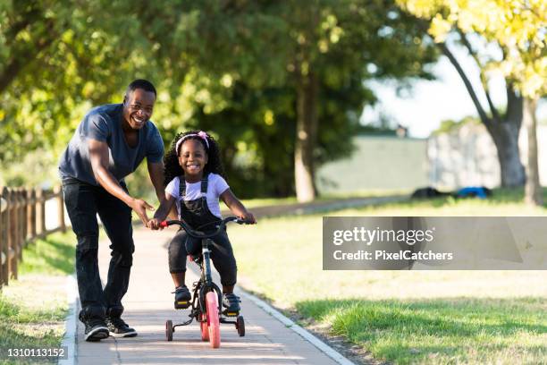 smiling little girl riding tricycle with father in park - girl bike stock pictures, royalty-free photos & images