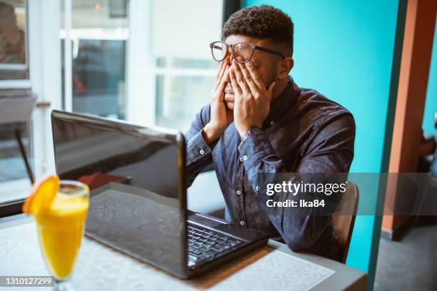 ラップトップで働く疲れて心配した若いアフリカ系アメリカ人男性 - 欲求不満 ストックフォトと画像