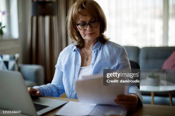 ernstige rijpe vrouw die laptop gebruikt om thuis te werken - comparison stockfoto's en -beelden