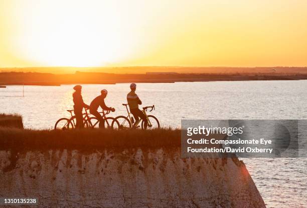 cyclists taking a break looking out to sea at sunset - david cliff stock pictures, royalty-free photos & images