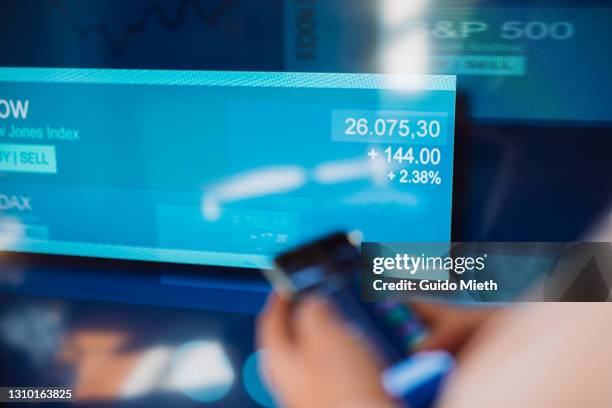 woman trading stock with mobile app in front of stock exchange screen. - certificato azionario foto e immagini stock