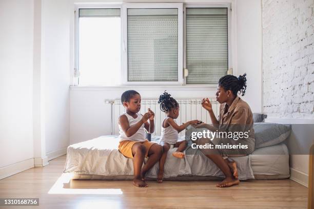 african-american mother, son and daughter sitting on the bed while the mom is giving them snacks - kids in undies stock pictures, royalty-free photos & images