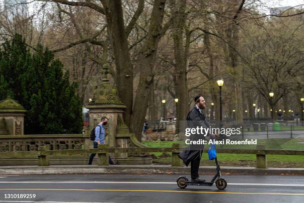 Man without a mask rides an electric scooter in the rain in Central Park on March 31, 2021 in New York City. Electric scooters and throttle...