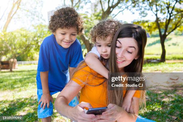 kinderen met moeder die technologie tijdens een onderbreking in het park gebruiken - family law stockfoto's en -beelden