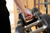 Hands of an Asian man taking dumbbells from a rack