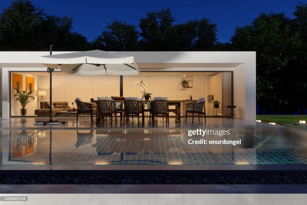 Exteriör av lyxig modern villa på natten med pool, uteplatsbord och stolar